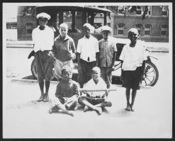 A group of adolescent boys gathered around an old fashioned car in Southwest. Most of the seven boys appear to be African American, but at least one is white. The picture is from 1924. A group of adolescent boys gathered around an old fashioned car in Southwest. Most of the seven boys appear to be African American, but at least one is white. The picture is from 1924.